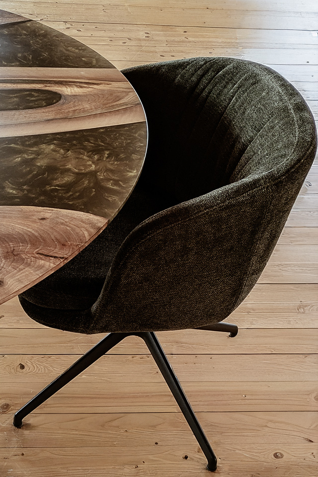 Am runden Esstisch aus Nussbaum mit Epoxidharz in spezieller Liebwerk Farbmischung steht ein bequemer Polsterstuhl