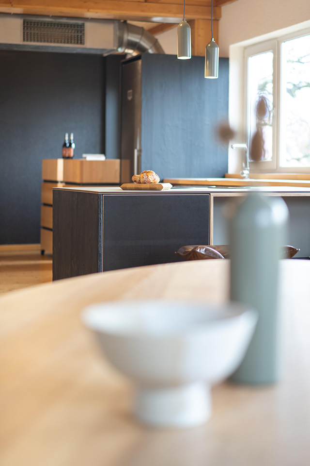 Der helle Tisch aus Esche wurde als starker Kontrast zu dunklen Küche von Liebwerk Schreinerei geplant.